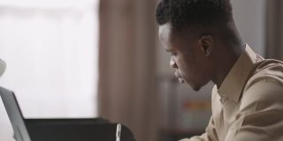 成年黑人男学生正在网上学习，用笔记本电脑在线听课，做笔记，在笔记本上写字