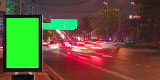一个在繁忙的夜晚街道上的绿屏广告牌。时间流逝。交通与城市景观概念。