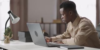 一名黑人青年在笔记本电脑上观看和收听在线学习研讨会，在家通过网络自学，做笔记
