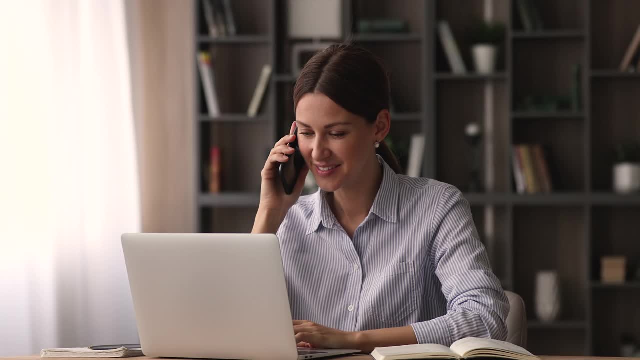 快乐的年轻35岁的女商人在电话上聊天，在电脑上工作。