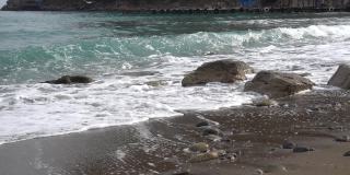 在克里米亚的诺维斯韦(Novy Svet)村的荒芜沙滩上，一股纯净的黑海海浪拍打着一块石头。早春多云