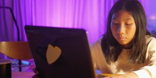 快乐的亚洲女孩在晚上用笔记本电脑在家里用LED灯，生活理念。