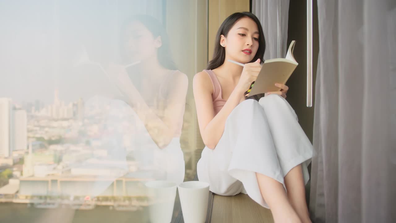 亚洲女性在酒店休闲放松，迷人的休闲布女坐在窗凳上周末活动宁静幸福的早晨时间
