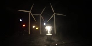 电力在自然界或清洁能源概念。风力发电机在晚上生产替代能源。由替代能源供电的发光灯泡。创意小微缩装饰。有选择性的重点