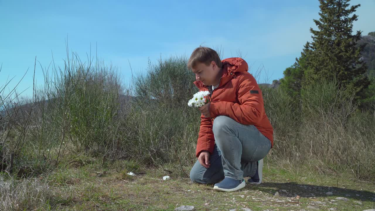 早春时节，一名年轻男子穿着羽绒服，在草坪上为心爱的人收集了一束白色的雏菊。让你爱的人高兴或祝贺他们的小惊喜。