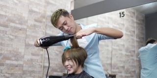 亚洲发型师在发廊为她的顾客吹头发