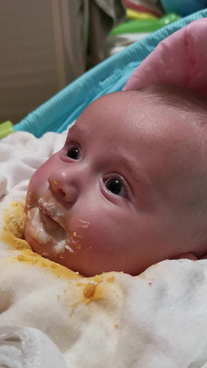 宝宝吃东西，弄得一团糟。三个月大的婴儿在吃晚饭。看着摄像机。