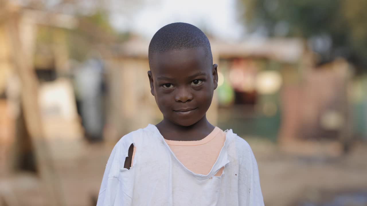 贫穷，不平等，一个贫穷害羞的非洲黑人男孩在贫民窟周围看着照相机微笑的肖像