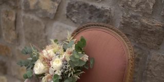 精致的新娘花束和精致的织物放在靠墙的粉红色扶手椅上