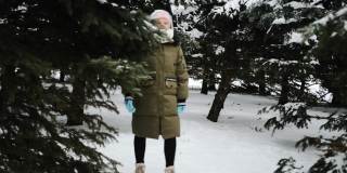 一个女孩在冬天里穿着暖和的冬装走在森林里，周围有许多树在雪地里