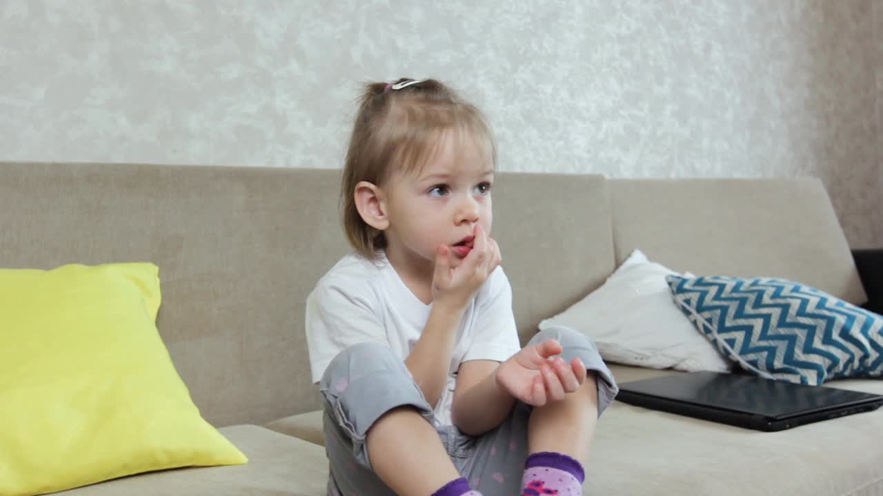 一个小女孩坐在家里的沙发上，一边看着前方，一边咬着指甲。孩子的坏习惯