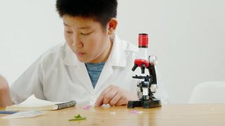 亚洲小学生穿着实验服一起在科学课上使用显微镜，教育理念。视频素材模板下载