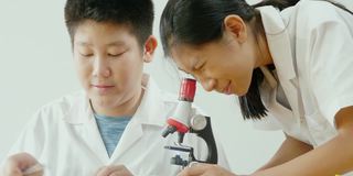 亚洲小学生穿着实验服一起在科学课上使用显微镜，教育理念。