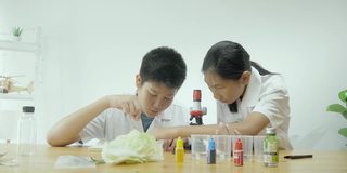 亚洲小学生穿着实验服一起在科学课上使用显微镜，教育理念。