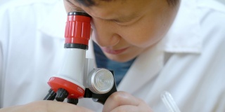 亚洲男生穿着实验服在科学课上使用显微镜，教育理念。