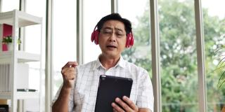 成熟的男人戴着耳机听音乐，通过耳机和数码平板电脑在客厅里唱歌。
