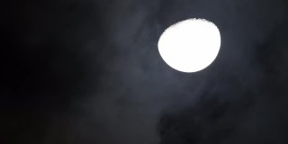 夜晚，月亮挂在黑色的天空上，乌云从它上面掠过。阴森可怕的夜空，乌云密布，满月皎洁。