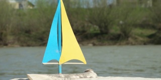 沙滩上是自制的玩具帆船，背景是现在的山河