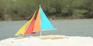 沙滩上是自制的玩具帆船，背景是山河