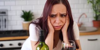 一个不幸的年轻女子喝红酒后头疼。成年女性在厨房喝酒时感觉不好
