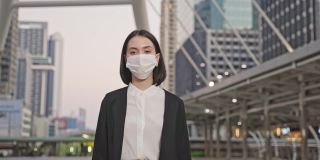 肖像亚洲年轻美丽的女商人站在户外与快乐和自信的脸在城市。聪明的工作妇女脱下或戴上防护口罩，以防止感染新冠病毒。