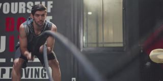 白种年轻英俊活跃的男性运动员或运动员在健身房或健身俱乐部用格斗绳做双波运动来减肥，炸脂肪，塑形肌肉，增加灵活性。
