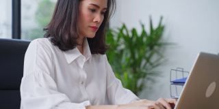 亚洲年轻女商人工作在一个新的正常的生活方式概念的电脑在办公室。女性经理在公司办公室单独使用笔记本电脑发送文件。
