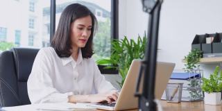 亚洲年轻女商人工作在一个新的正常的生活方式概念的电脑在办公室。女性经理在公司办公室单独使用笔记本电脑发送文件。