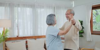 亚洲活跃的老年夫妇微笑感觉在爱和幸福的家。年迈的爷爷和奶奶在客厅里一起跳舞。老年人的家庭关系和活动概念