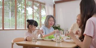 快乐的亚洲大家庭一起在餐桌上吃午餐。小女儿喜欢和爸爸、妈妈、爷爷奶奶一起吃东西。多代关系和家庭活动