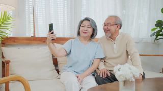 亚洲美丽的老女人和老男人夫妇在家里用手机和儿子、女儿视频通话，和孙子孙女聊天。祖父母对通过互联网交流感到高兴视频素材模板下载