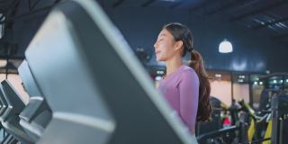 亚洲年轻运动员或女运动员在健身房或健身俱乐部锻炼以保持肌肉。一个活跃的美丽女性在运动服微笑，在跑步机上跑步燃烧卡路里。