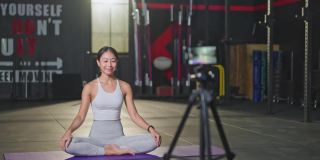 亚洲瑜伽女教师在健身房在线授课。该女孩在网上直播自己的课程，并通过智能手机录制，以便在COVID - 19疫情期间健身房关闭时将学生隔离在家。