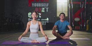 亚洲瑜伽美丽的女老师在健身房教强壮的白人男子。女孩伸展手臂和身体带领学生在做核心瑜伽姿势和健身锻炼之前在后面。
