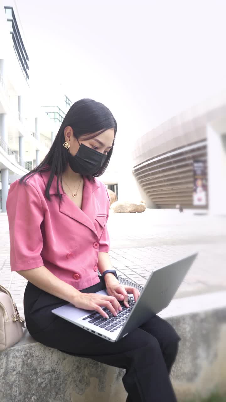 美丽的亚洲女人戴着防护口罩使用笔记本电脑在户外