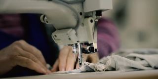 浅景深(选择性聚焦)镜头，一位在纺织厂电动缝纫机上工作的高级妇女的双手。
