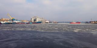 无人机拍摄的画面显示，在冰冻水域的货运站上有船只，码头上有港口起重机和粮食储存罐