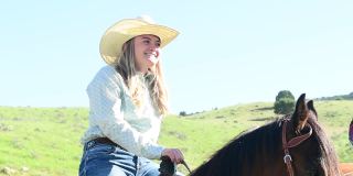 美丽自信的年轻美国女人在牛仔帽骑马在犹他州