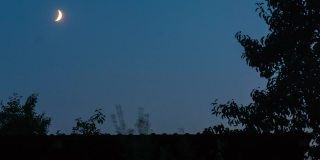 新月在树和屋顶的剪影前顺着天空移动