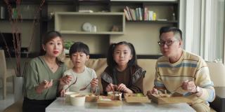 亚洲华人年轻家庭周末在客厅的电视前享受外卖食物