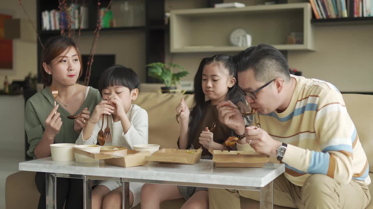 亚洲华人年轻家庭周末在客厅的电视前享受外卖食物