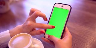 用绿屏智能手机的女人。女人的手在手机上滚动页面的特写视频。色度键。垂直