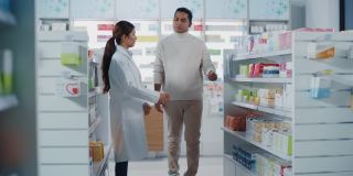 药店:女性亚洲药剂师帮助印度男性客户与推荐，并建议购买药物，药物，维生素。现代药店货架与保健产品