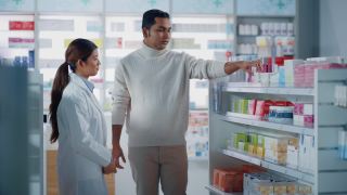 药店:女性亚洲药剂师帮助印度男性客户与推荐，并建议购买药物，药物，维生素。现代药店货架与保健产品视频素材模板下载