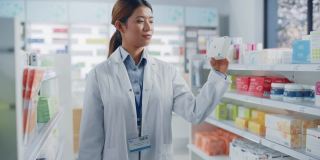 药店:亚洲职业女性药剂师的肖像拿着模拟模板药品包装跟踪标记，看着相机，微笑。专家推荐最佳产品