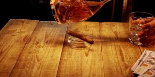 男人的手的特写，谁是坐在木桌和倒威士忌在一个缓慢的杯子