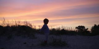 小男孩的剪影站在引人注目的紫色日落天空背景