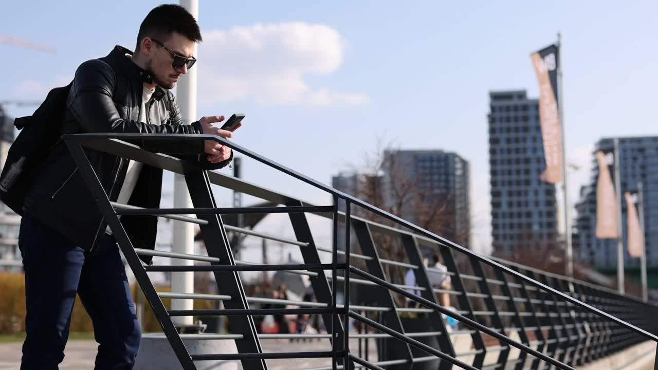 一个年轻人在城市的河边用手机发短信