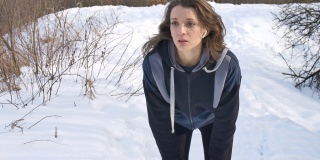 春天或冬天的肖像，年轻的运动女孩在公园里跑步，穿着深色运动服在树上与雪的背景。健康的生活方式的概念。