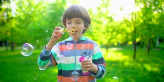 特写的快乐可爱的小男孩吹，有乐趣与肥皂泡在公园。小朋友在阳光明媚的夏日里慢悠悠地在外面玩耍，节日快乐，假期，童年，夏日时光